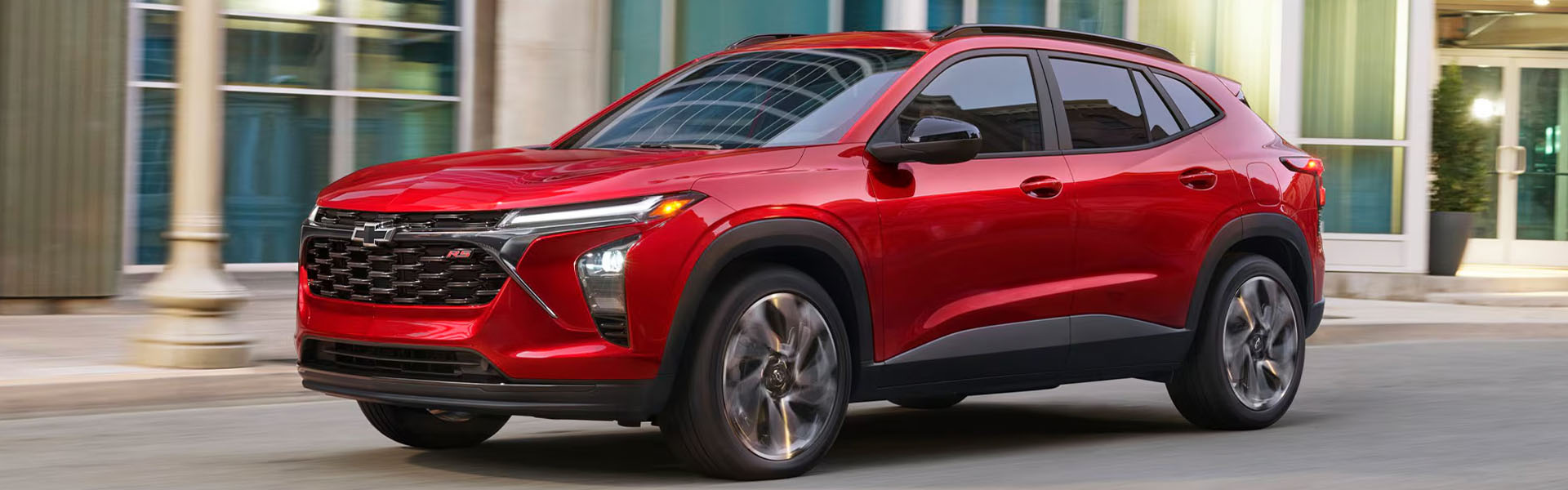 Red Chevrolet Trax driving on city road.